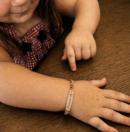 Child wearing a gold bracelet with an engraved message on a wooden surface
