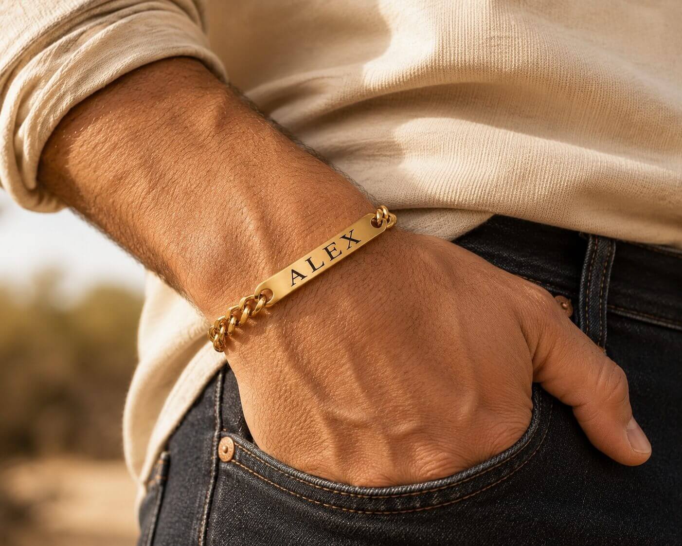 Gold bracelet with 'ALEX' engraved on a wrist, blurred background