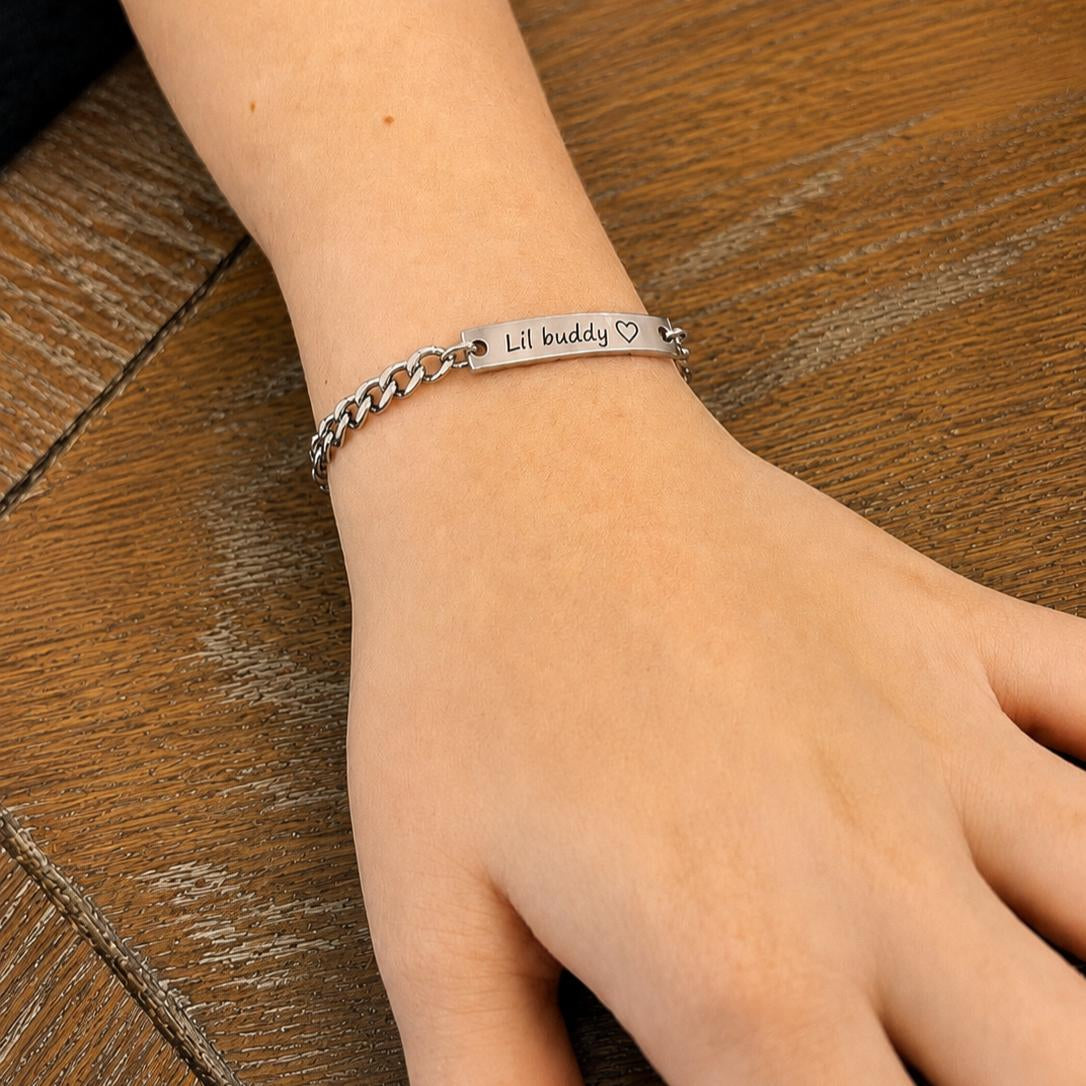 Silver bracelet with 'Lil buddy' text on a wrist against a wooden background